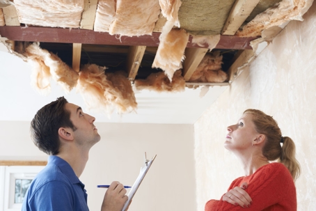 Man with clipboard and woman look up at a collapsed ceiling